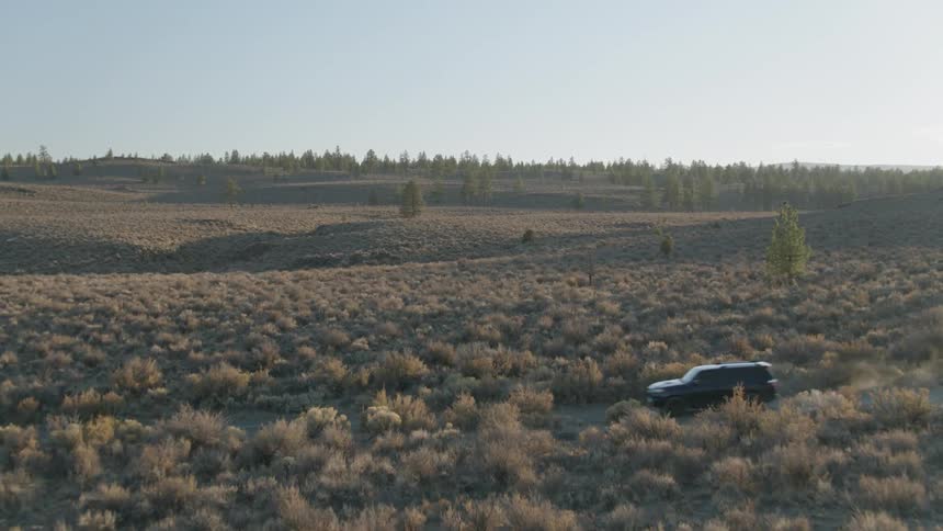 A car driving on a rural road kicks up dust on a sunny day