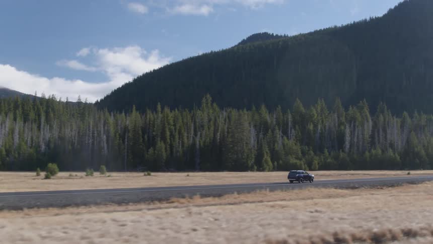 A vehicle drives by forest trees and mountains