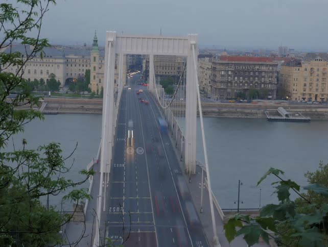 Boats travel under a city bridge as vehicles travel above