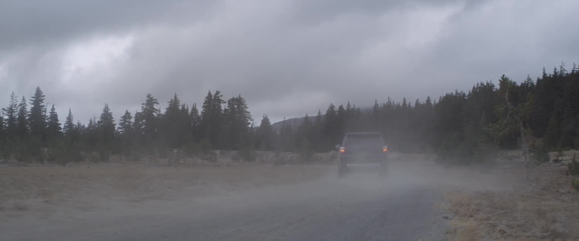 An suv is driving fast on a rural dirt road as storm clouds gather in the sky