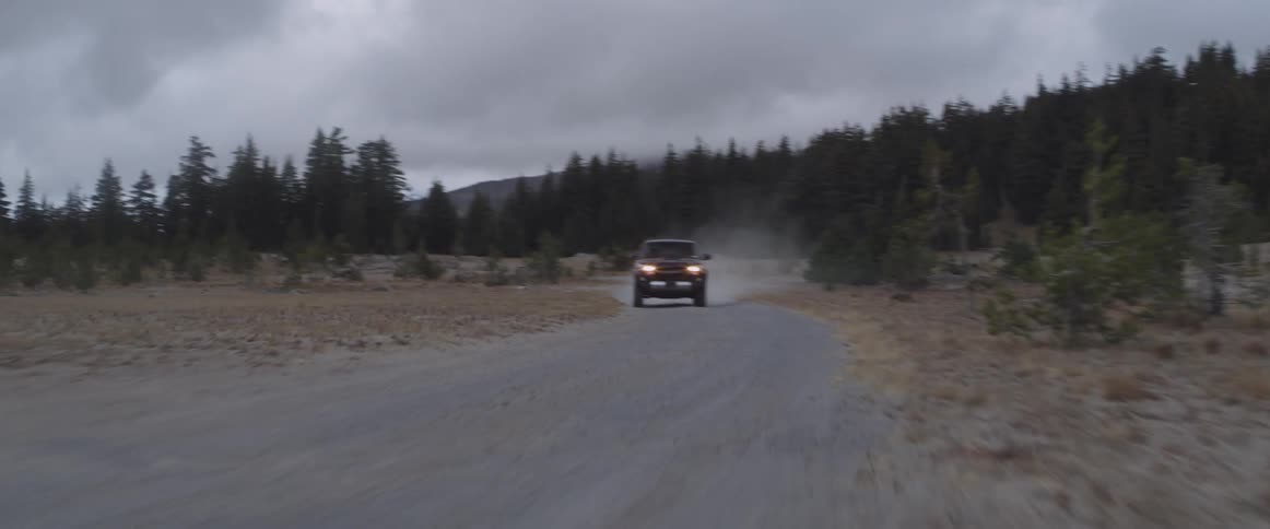 An suv is driving fast on a rural dirt road at dusk