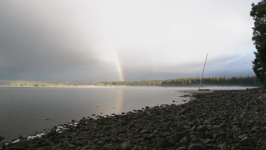A rainbow arcs out of the clouds near the lake