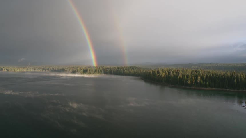 A rainbow extends above forest trees and a lake