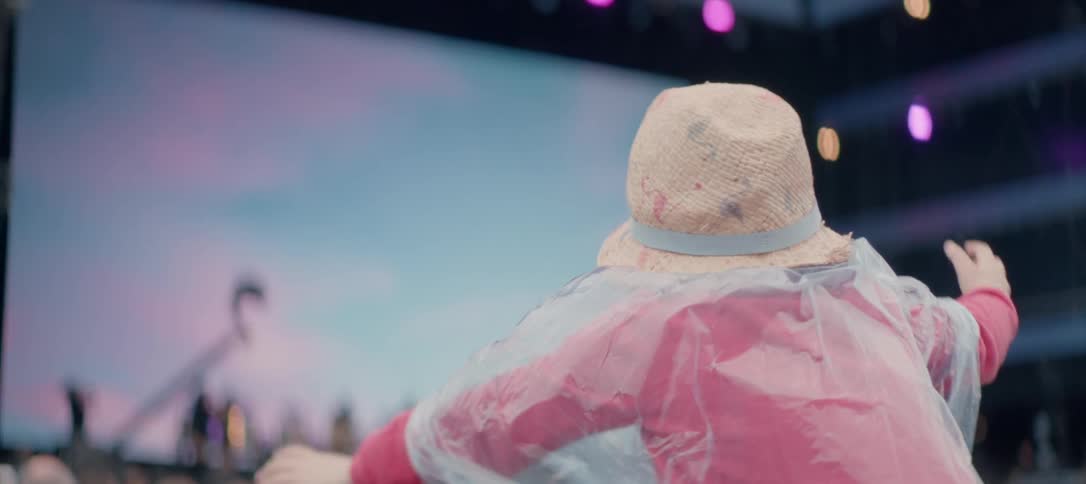 A concertgoer waves their arms in a rain poncho