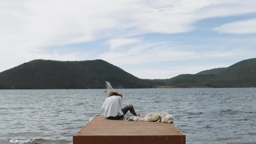 A woman sits on a dock on the water with her dog