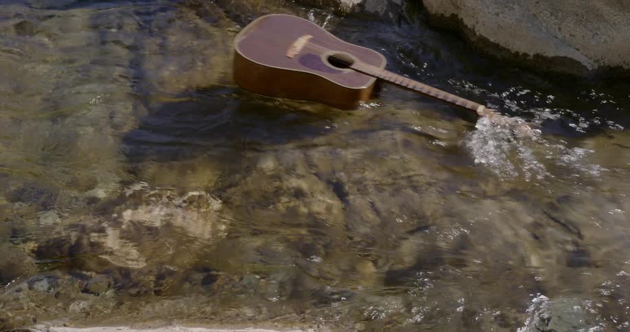 A guitar floats over rocks in a clear stream on a sunny day