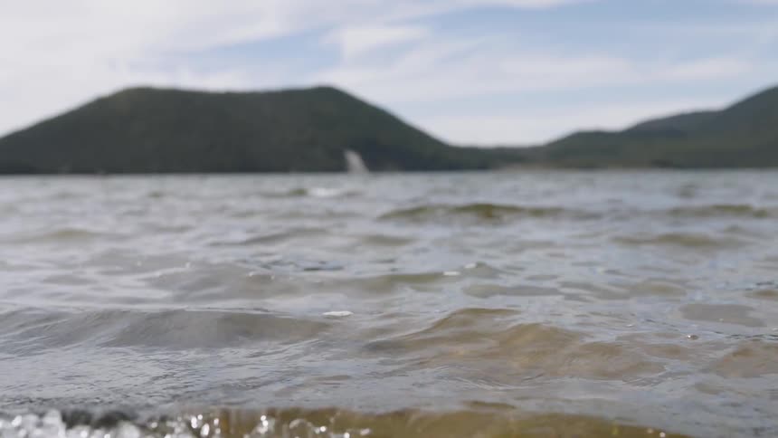 Small waves roll in with a hill in the distance
