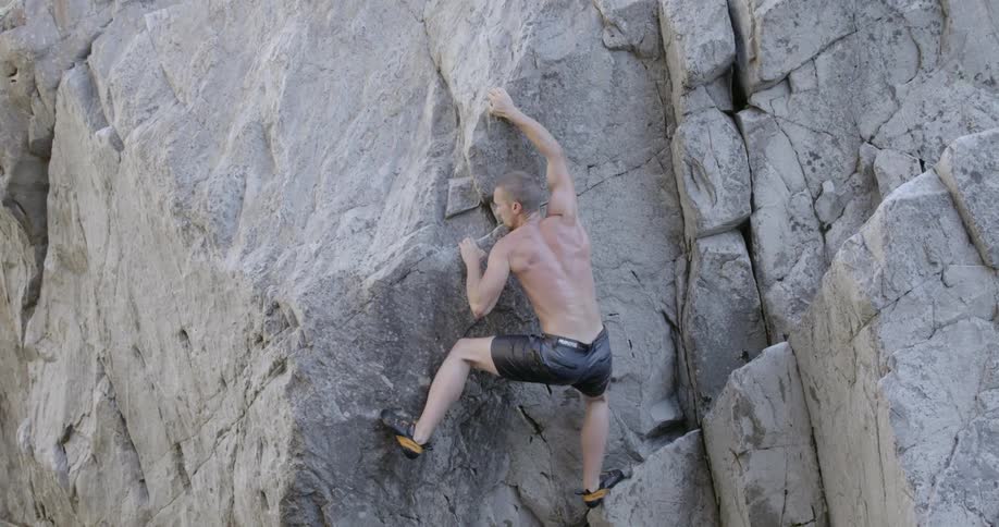 A man trying to climb a rock wall falls off into a pool of water