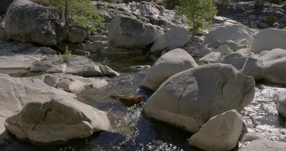 A guitar is floating in a stream between rocks and boulders during the day