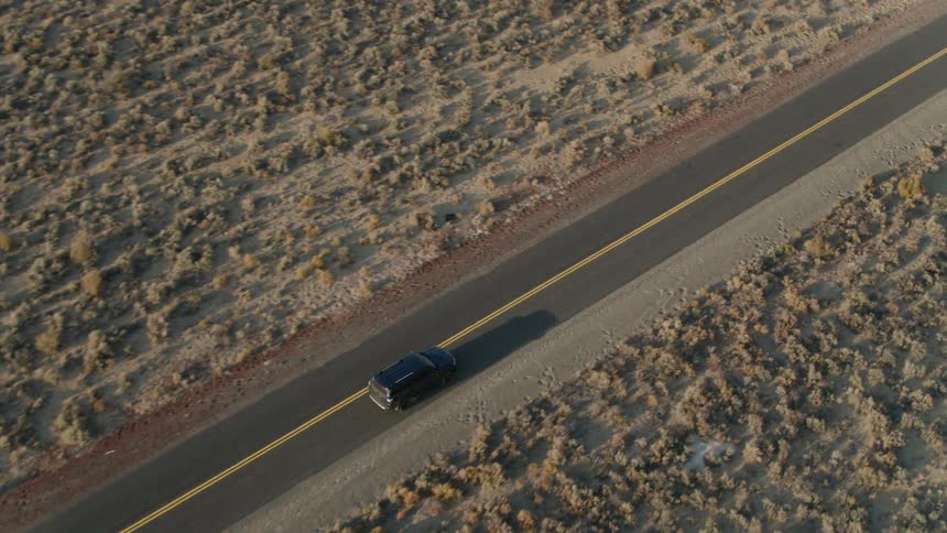 A vehicle drives on a rural desert road