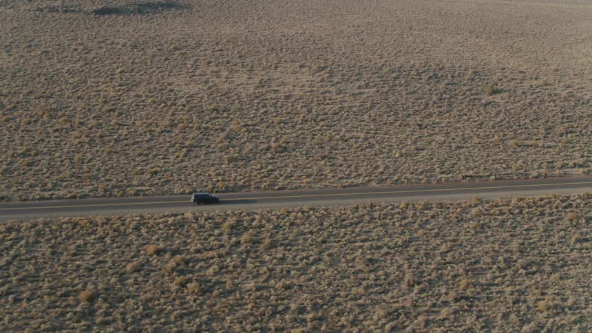 Vehicle drives down a lone road in the middle of the desert