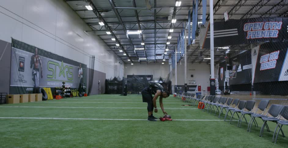 A man sets his shoes and football down in an indoor field