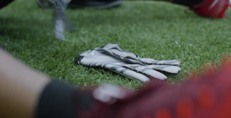 An athlete puts on gloves while sitting on grass