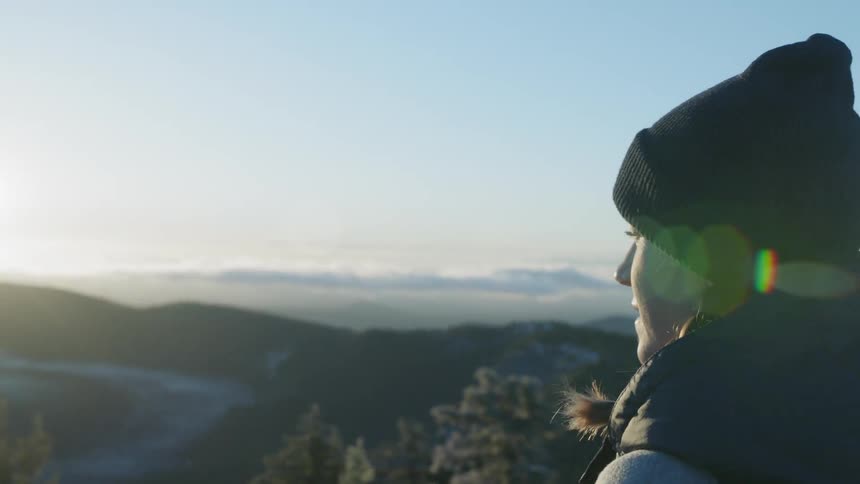 A woman looks out over the mountain valley below at sunrise