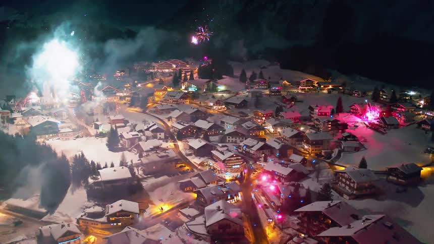 Fireworks are exploding in the sky over a village during a winter night