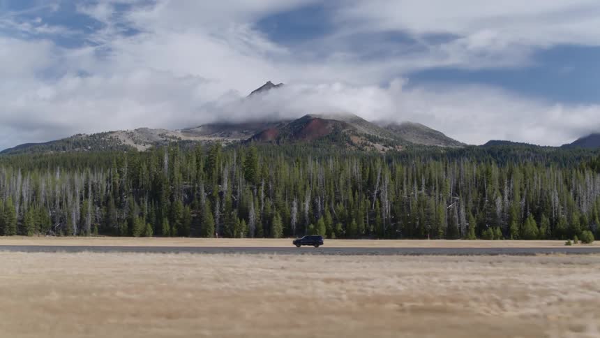 An suv drives past trees and mountain on a rural road