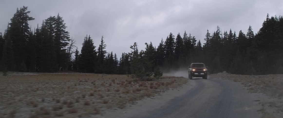 An suv travels on a dirt road with headlights on