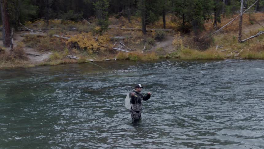 Person stands in the middle of a river fly fishing