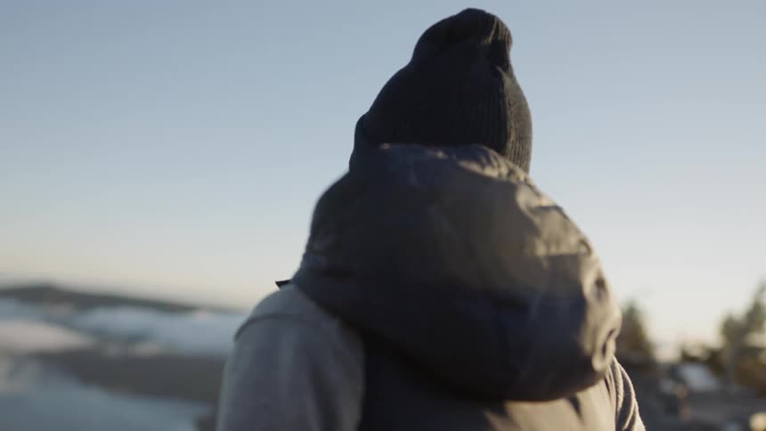 Woman wearing a backpack stands outside on a sunny day