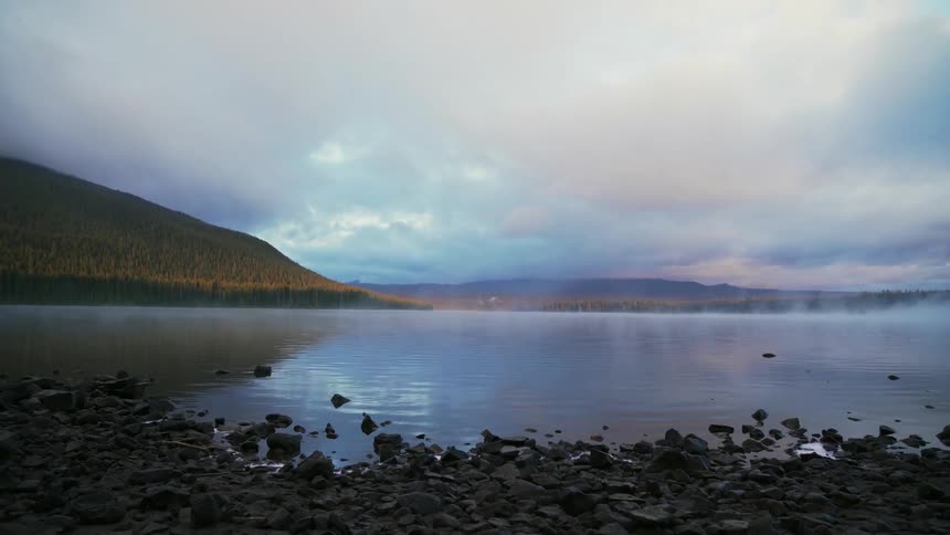 Fog is lingering on a lake in a natural setting at dawn