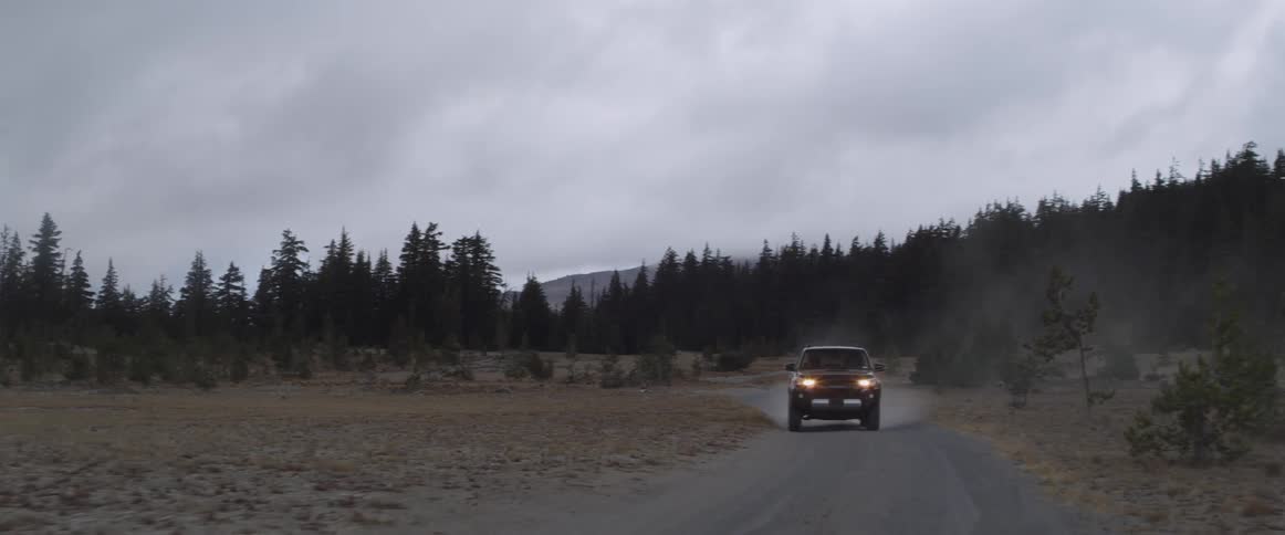 A vehicle drives on a dirt forest road