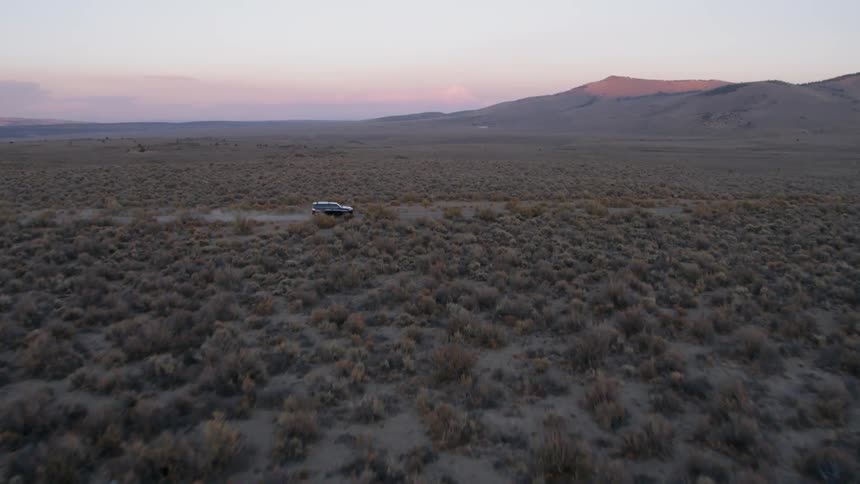 Car drives on a country road surrounded by brushy plains