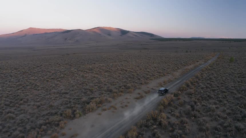 A vehicle drives on a rural desert road at sunset
