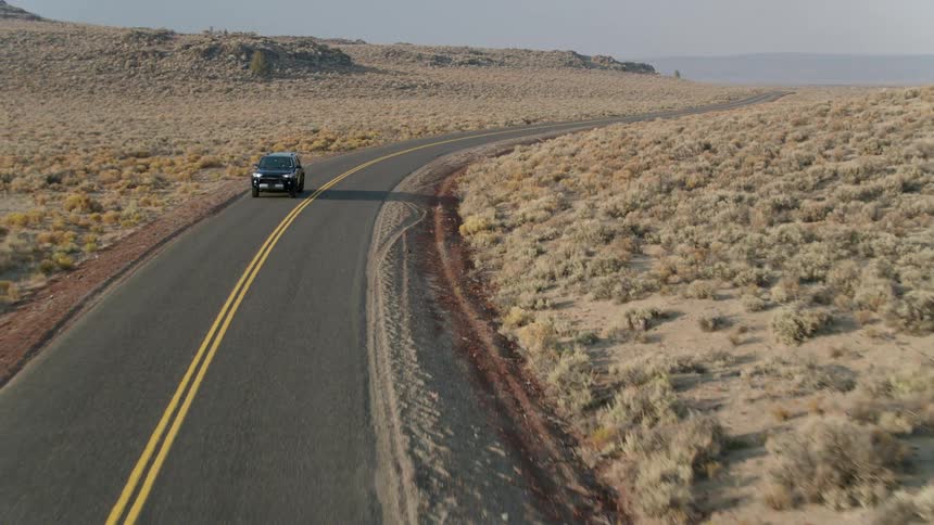 Jeep drives down a country road surrounded by hilly brushy plains