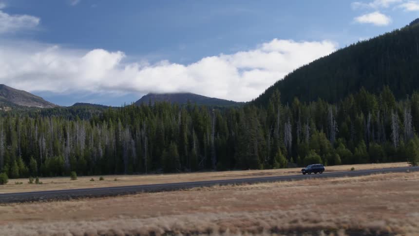 A car travels along a road with lots of trees and mountains in the distance