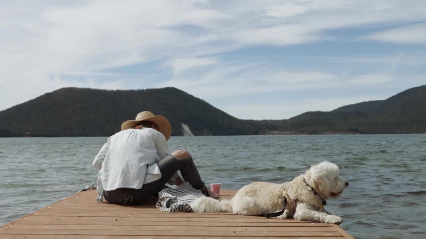 A woman and dog sit on a lake dock