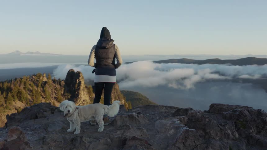 A woman and her dog stand on a rocky ledge