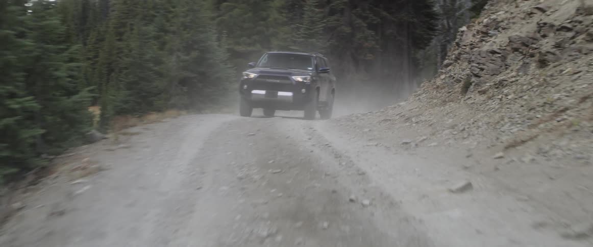 An suv is driving on a dirt road through a forest at dusk
