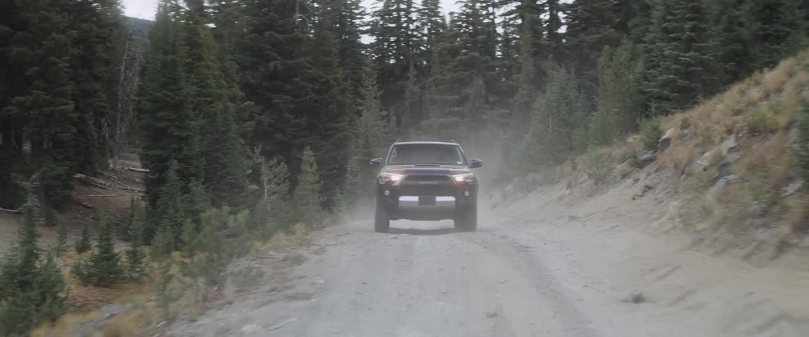 A vehicle drives on a dusty mountain road
