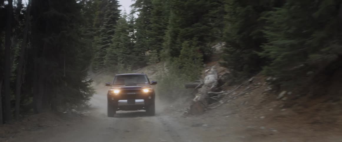 Vehicle driving down a dirt road through a forest