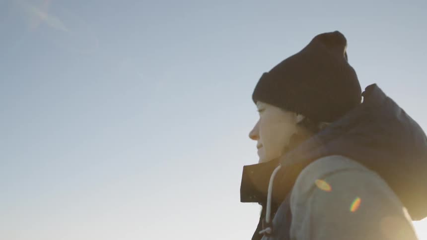 A woman is smiling as she stands looking out at a view on a cold day