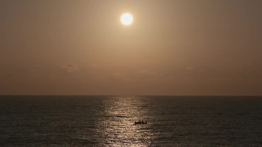 Two people sit in a small boat on the ocean at sunset