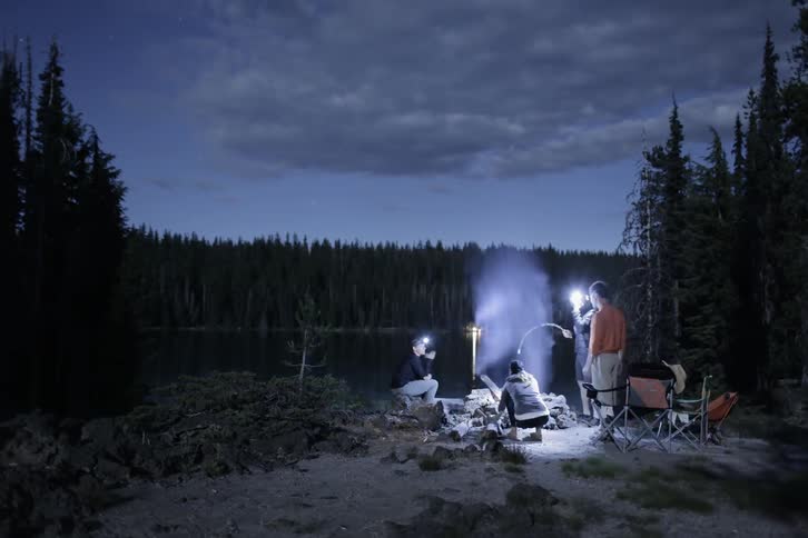 People standing in front of a fire near a lake at night