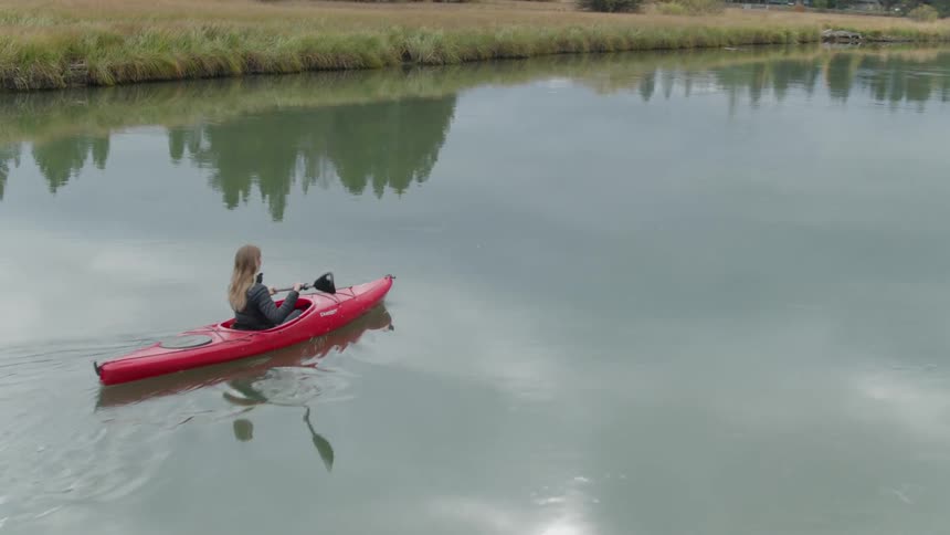 A woman is kayaking in a river on a cloudy day