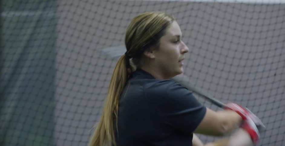 A woman swings a baseball bat in front of the catch net