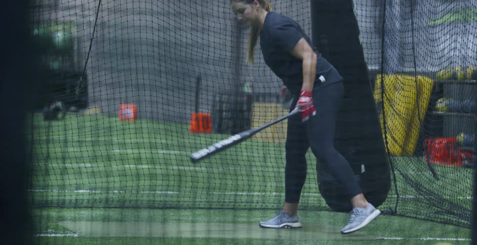 A woman holding a softball bat stands up and sets for a pitch