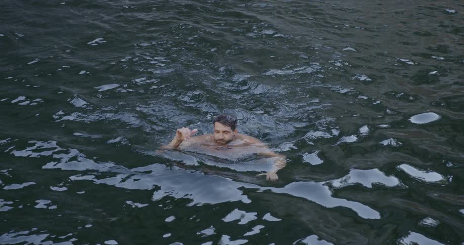 A man is smiling and throwing a hand sign as he swims in a natural pool