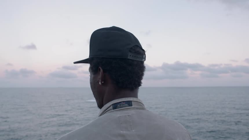 A man is standing and looking out at the ocean with a friend at dusk