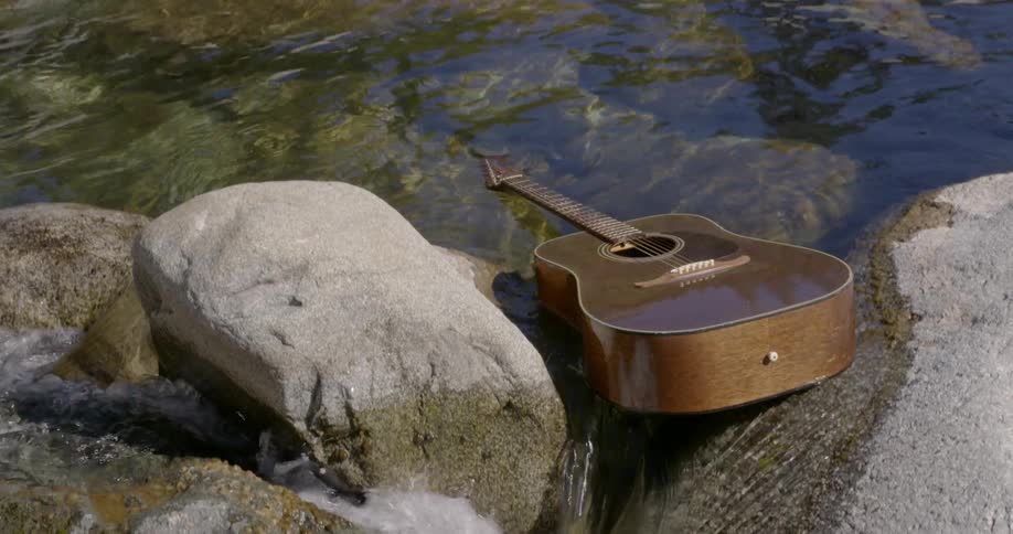 A guitar floats on a river and falls over boulders