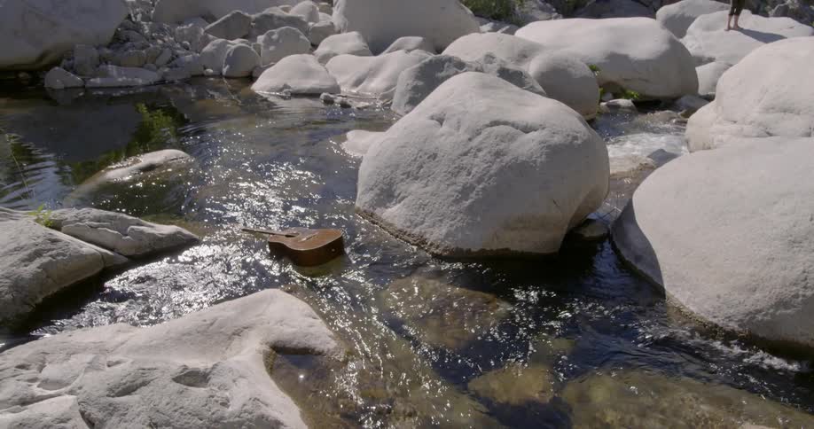 A guitar floats down a stream in the mountains on a sunny day