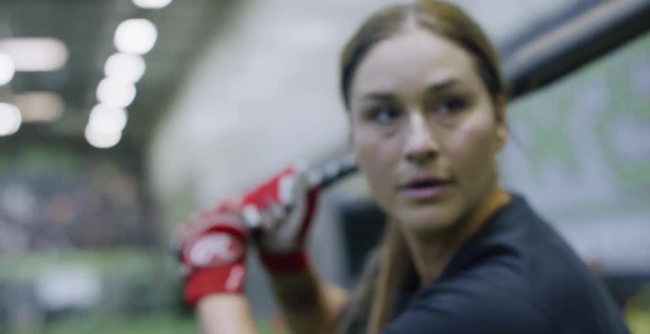 A woman softball player hits the ball indoors