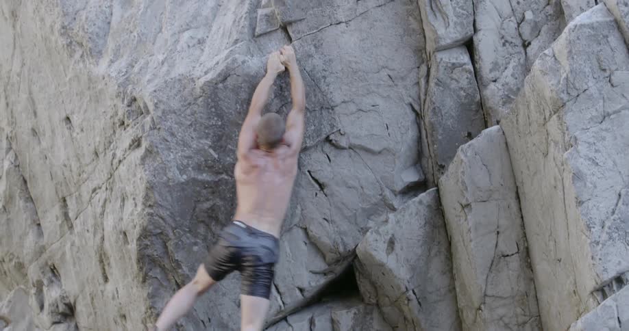 A man climbing a rock wall reaches for a hold and falls
