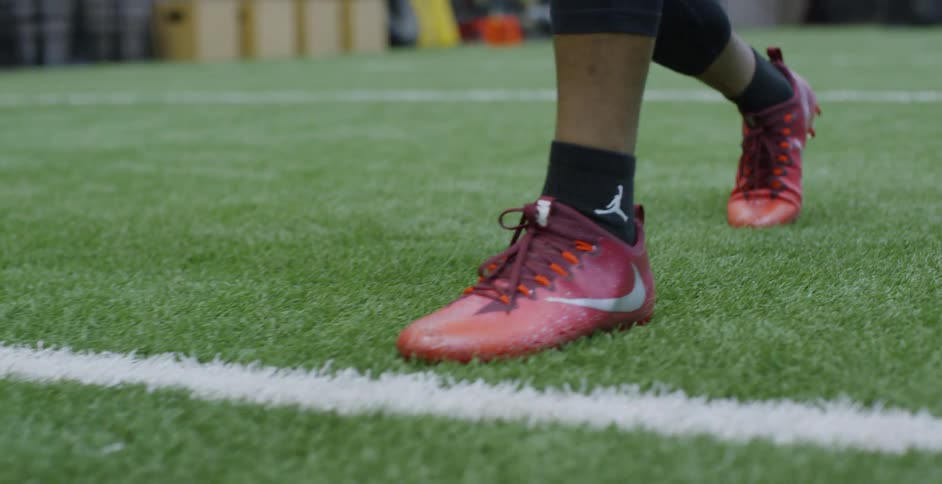 A man wearing red football cleats is running drills