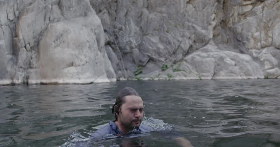 A man is dunking himself in the water next to a granite rock wall