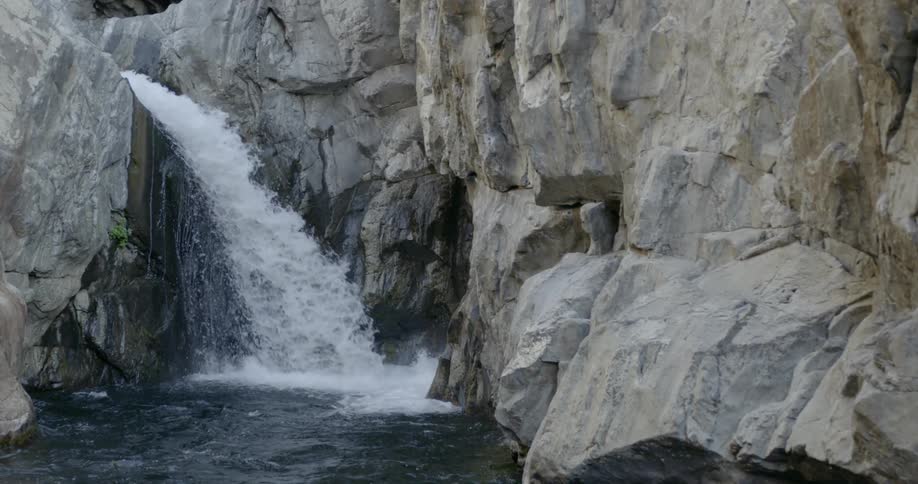 A waterfall is cascading over a ledge and into a gorge during the day