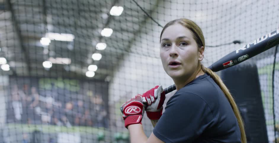 A woman hits a baseball in a batting cage
